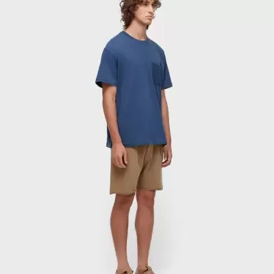 Homem com t-shirt azul e calções castanhos claros em fundo branco