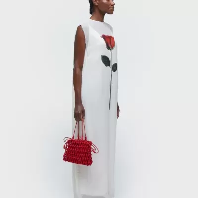 Vestido branco comprido com estampa de rosa vermelha e mala vermelha em modelo contra fundo branco