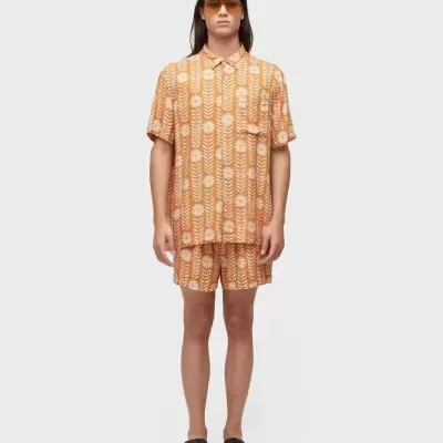 Homem com conjunto laranja e branco com padrão floral, óculos de sol e chinelos pretos