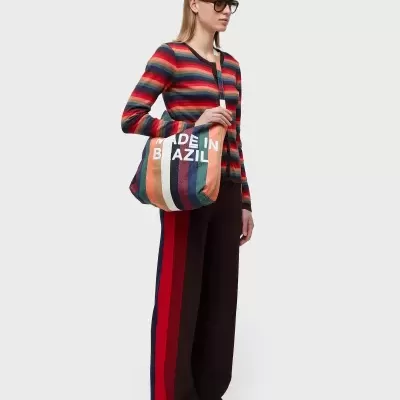 Modelo com camisola e calças às riscas, óculos escuros, e mala de tecido com texto 'MADE IN BRAZIL'.