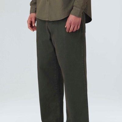 Calças largas verdes escuras com bainha irregular, camisa verde-oliva e sapatos bege