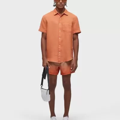 Homem com camisa e calções laranja, óculos de sol e mala pequena branca