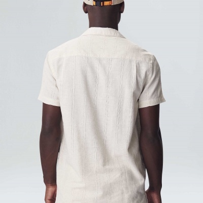 Homem de costas com camisa e calças curtas bege e boné bege com aba preta