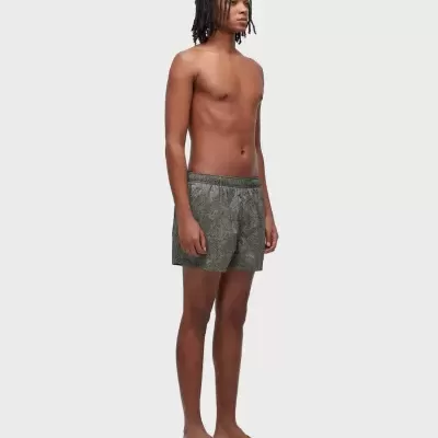 Pessoa com calções de banho cinza com padrão geométrico e chinelos castanhos