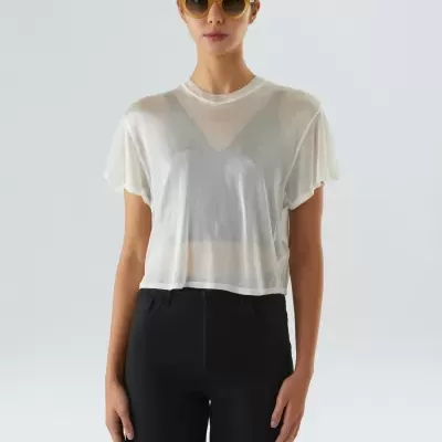 Mulher com óculos de sol castanhos, camisa branca transparente e calças pretas