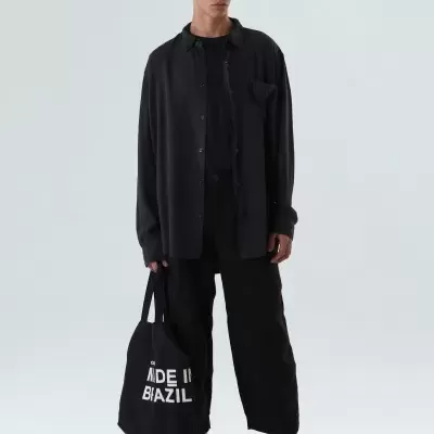 Homem jovem vestido de preto segurando sacola preta com texto branco em fundo branco