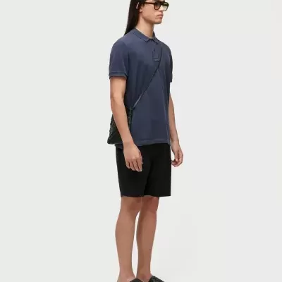 Homem vestido com camisa polo azul, calções pretos, chinelos pretos texturizados e óculos escuros