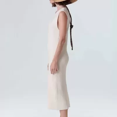 Mulher de perfil com vestido creme, chapéu de palha e sandálias bege