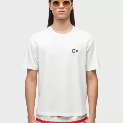 Homem com t-shirt branca e calções vermelhos com faixas brancas a usar óculos de sol amarelos