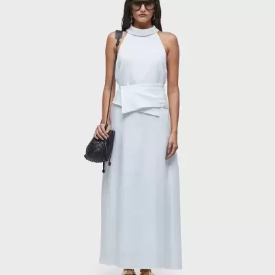 Vestido longo branco com cinto largo, mochila preta e sandálias castanhas.