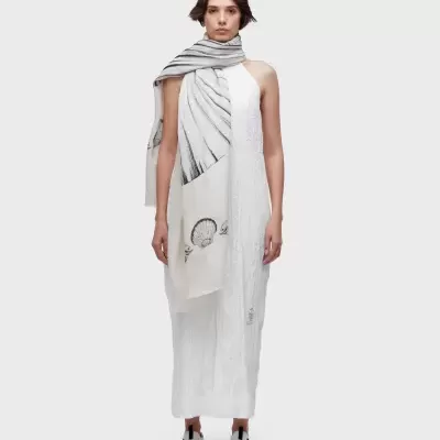 Pessoa com vestido branco texturizado e lenço branco com padrão de conchas e linhas pretas.