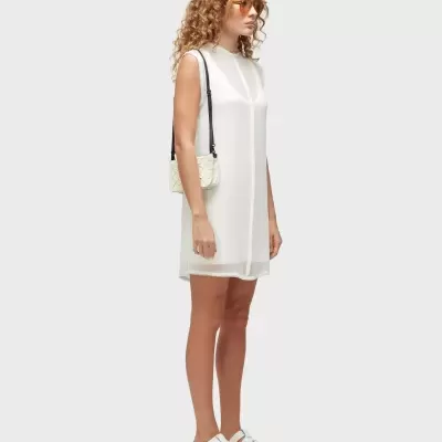 Mulher com vestido branco, bolsa bege e sandálias brancas