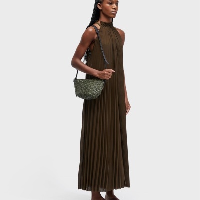 Mulher com vestido plissado castanho e mala verde de padrão escamas
