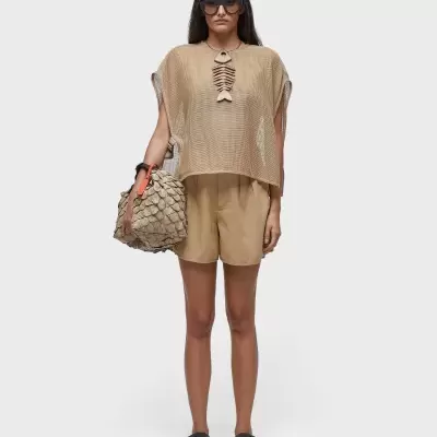 Mulher com roupa bege, mala texturada e sandálias pretas