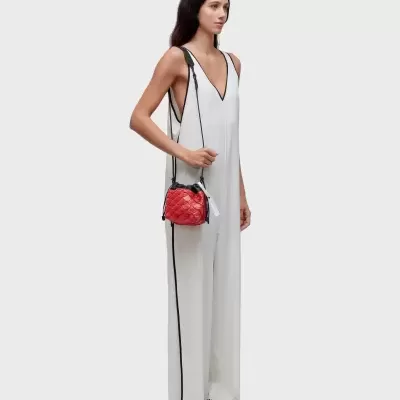 Mulher vestindo macacão branco com detalhes pretos, sapatilhas pretas e brancas, segurando bolsa vermelha acolchoada.