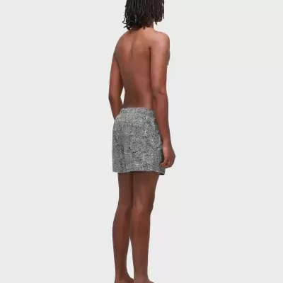 Pessoa de costas com calções de banho cinzentos e padrão branco, com chapéu bege, em fundo branco