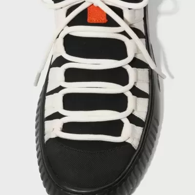 Ténis preto e branco com atacadores brancos e detalhe laranja