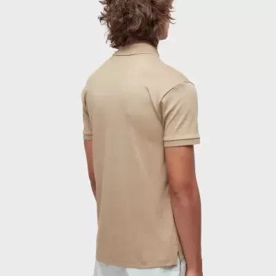 Homem de costas a vestir polo bege e calções brancos num fundo cinzento claro