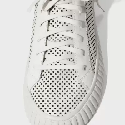 Ténis branco com perfurações pretas, sola texturizada e atacadores brancos