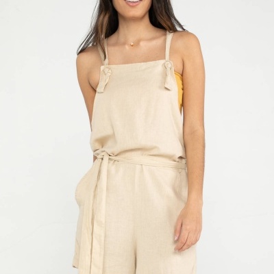 Macacão curto bege com cinto e alças finas usado por mulher em fundo branco