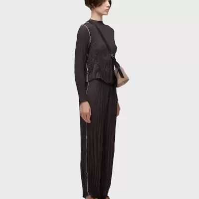 Modelo com fato preto texturado e sandálias castanhas e mala bege