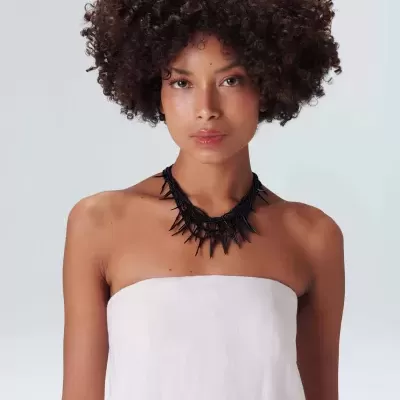 Colar preto de picos em modelo com vestido branco e fundo cinzento
