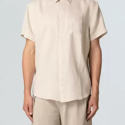 Camisa bege clara de manga curta com bolso e botões, usada com calças do mesmo tom