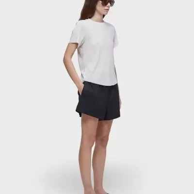 Mulher de perfil a usar t-shirt branca, calções pretos, chinelos verdes e óculos escuros