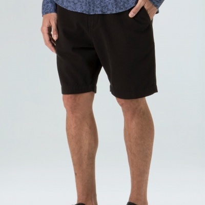 Homem a usar bermuda preta e camisa azul, de pé sobre fundo branco