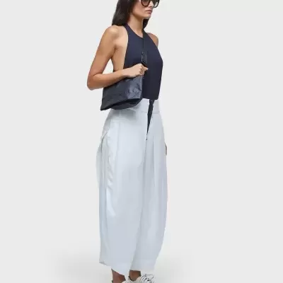 Mulher com top preto, calças brancas largas, ténis brancos, óculos escuros e mala preta