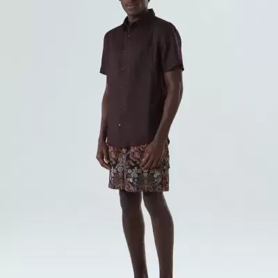 Homem com camisa castanha, calções com padrão floral e ténis azuis