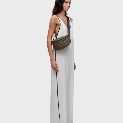 Mulher com vestido branco longo e mala transversal verde-oliva acolchoada