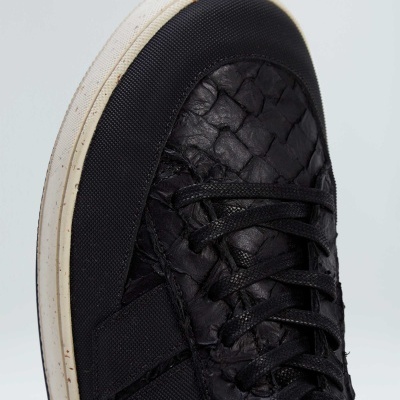 Tênis desportivo preto com padrão trançado e sola branca sobre fundo claro