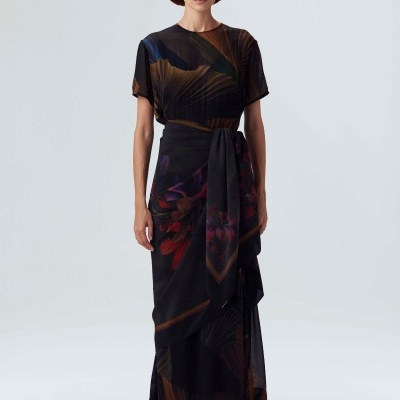 modelo a usar vestido comprido escuro com padrão floral, chapéu castanho, óculos de sol e sapatos laranja