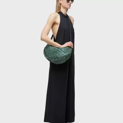 Mulher com macacão preto, óculos verdes, ténis e bolsa verde texturizada