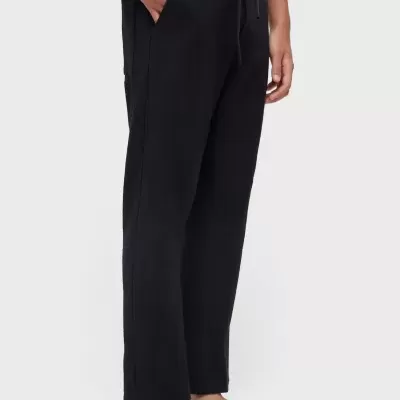 Calças pretas com bolso lateral e cordão na cintura, usadas com sandálias negras.