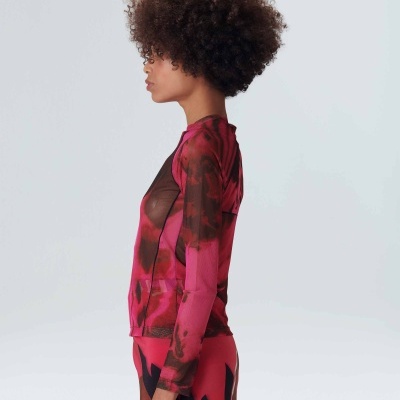 Mulher com blusa transparente vermelha, preta e rosa vista de perfil