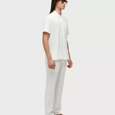 Homem com camisa branca, calças brancas, sandálias castanhas e óculos escuros