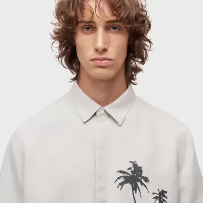 Camisa bege clara com palmeiras pretas no peito, modelo com cabelo castanho cacheado curto