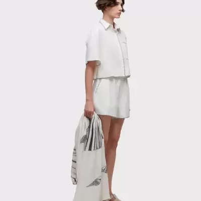 Conjunto branco com costura preta visível, lenço branco com padrão de conchas e sandálias bege