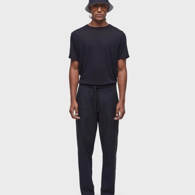 Homem vestido de preto com chapéu tipo pescador, t-shirt, calças e sapatos brancos num fundo branco.