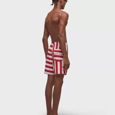 Homem com calções de banho de riscas vermelhas e brancas, chinelos pretos e óculos de sol.