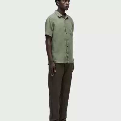 Homem com camisa verde e calças castanhas sobre fundo branco