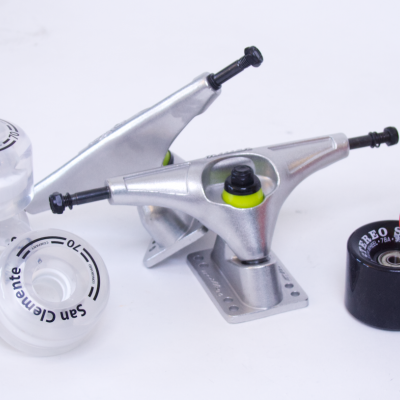 Peças para skate com truck metálico e rodas coloridas e transparentes sobre fundo branco.