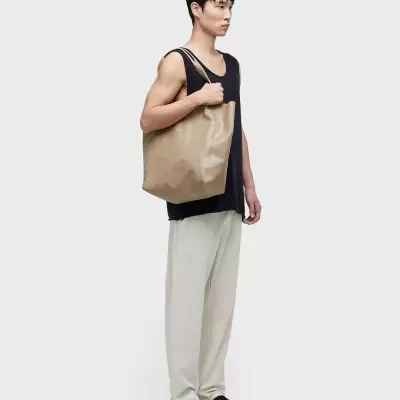 Homem com roupa casual preta e branca carregando bolsa tote bege