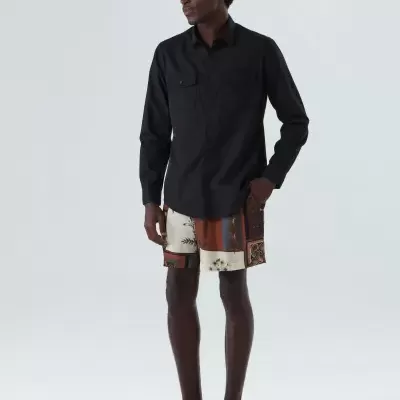 Homem com camisa preta de manga comprida e calções estampados em fundo cinza claro