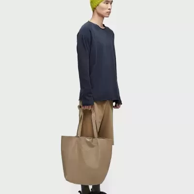 Homem com gorro amarelo, camisola preta, calças castanhas, segura mala bege