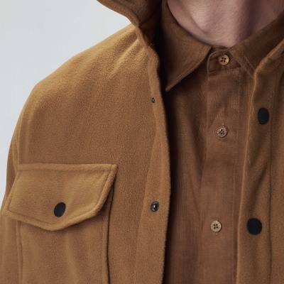 Detalhe de pessoa com camisa castanha e camisa/casaco felpudo castanho com bolsos e botões pretos