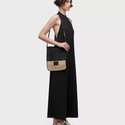 Mulher vestindo vestido preto longo, sapatos brancos e mala de ombro preta e bege.