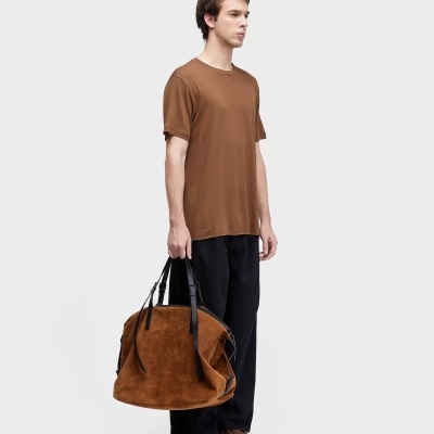 Homem com camiseta castanha, calças pretas e bolsa de camurça castanha